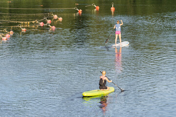 Young girls ride sub boards on the Pirita river in summer, rear view.