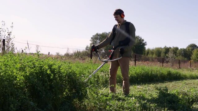 Man mows the green grass in the back yard with a gasoline lawnmower. Trimmer for cutting a garden plot