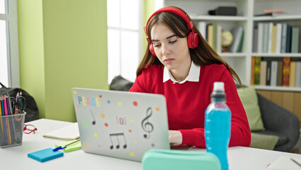 Young hispanic woman student using laptop and headphones studying at library university