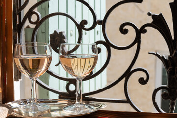 Fototapeta na wymiar French cold rose dry wine from Provence in glasses served on window frame with wrought iron grille and wooden shutters, Provence, France