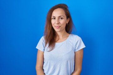 Obraz premium Brunette woman standing over blue background with hands together and crossed fingers smiling relaxed and cheerful. success and optimistic