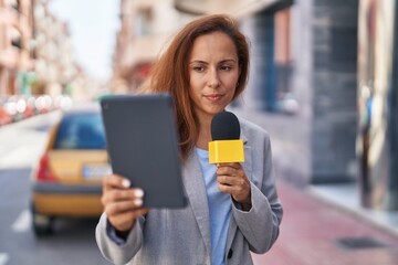 Young woman reporter working using microphone and touchpad at street