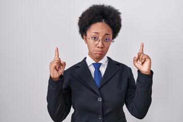 Beautiful african woman with curly hair wearing business jacket and glasses pointing up looking sad...