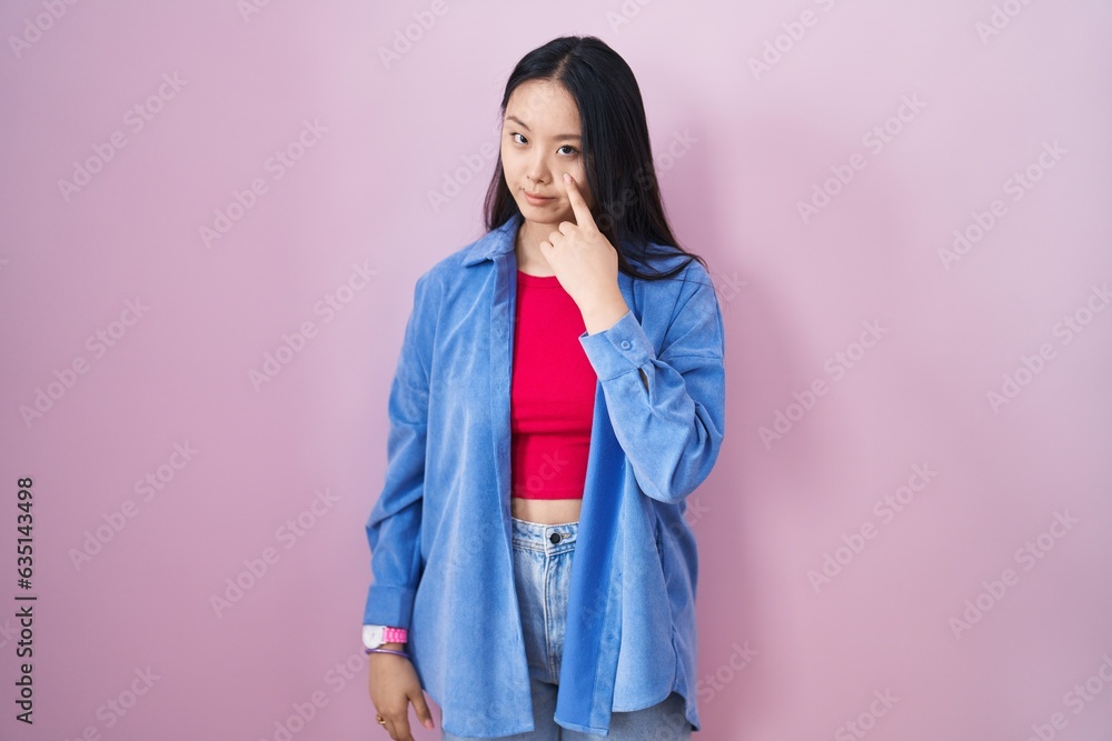 Sticker young asian woman standing over pink background pointing to the eye watching you gesture, suspicious