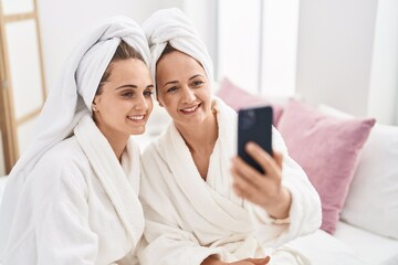 Two women mother and daughter wearing bathrobe make selfie by smartphone at bedroom - obrazy, fototapety, plakaty