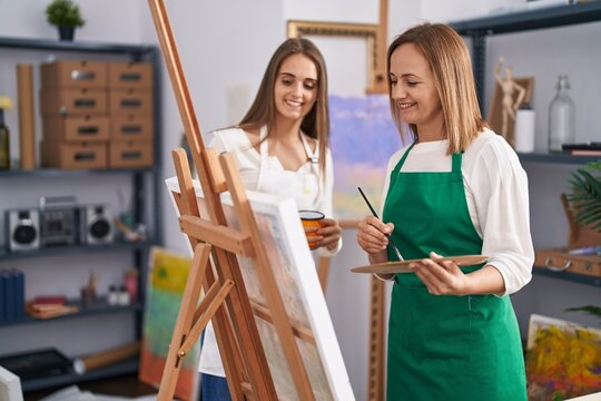 Two women artists smiling confident drinking coffee drawing at art studio
