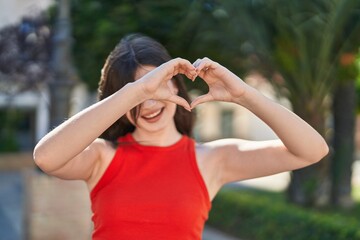 Young caucasian woman smiling confident doing heart gesture with hands at park