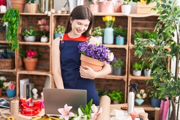 Young caucasian woman florist using laptop holding plant at florist