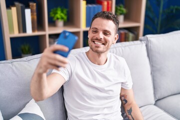 Young hispanic man make selfie by smartphone sitting on sofa at home
