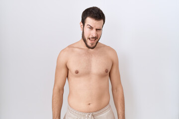 Young hispanic man standing shirtless over white background winking looking at the camera with sexy expression, cheerful and happy face.