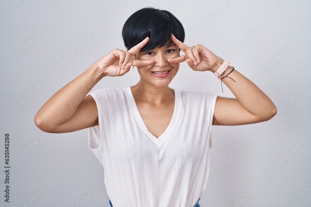 Poster young asian woman with short hair standing over isolated background doing peace symbol with fingers 