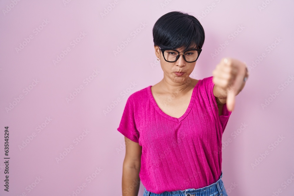 Canvas Prints Young asian woman with short hair standing over pink background looking unhappy and angry showing rejection and negative with thumbs down gesture. bad expression.