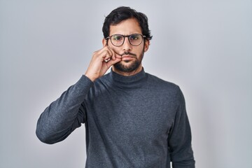 Handsome latin man standing over isolated background mouth and lips shut as zip with fingers. secret and silent, taboo talking