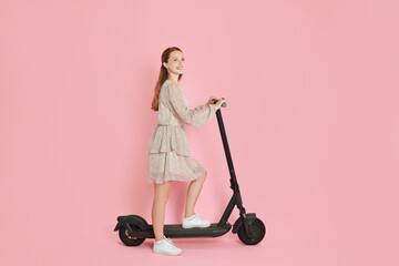 Happy woman with modern electric kick scooter on pink background