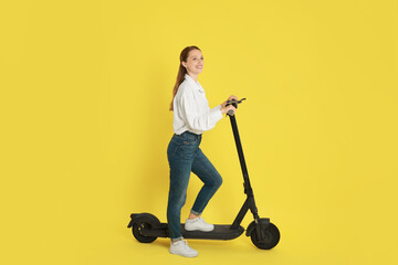 Happy woman with modern electric kick scooter on yellow background