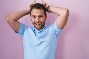 Hispanic man standing over pink background posing funny and crazy with fingers on head as bunny ears, smiling cheerful