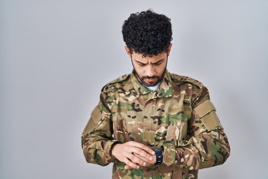 Arab man wearing camouflage army uniform checking the time on wrist watch, relaxed and confident
