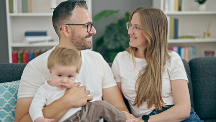 Family of mother, father and baby smiling sitting on the sofa at home