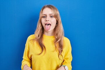 Young caucasian woman standing over blue background sticking tongue out happy with funny expression. emotion concept. © Krakenimages.com