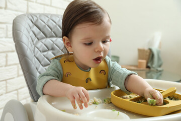Cute little baby eating healthy food in high chair indoors