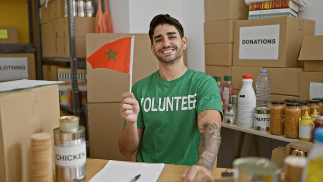 Young hispanic man volunteer smiling confident holding morocco flag at charity center