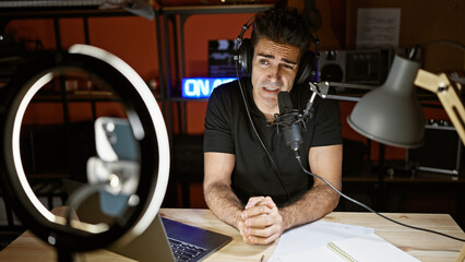 Young hispanic man speaking in a radio show recording video by smartphone at radio studio