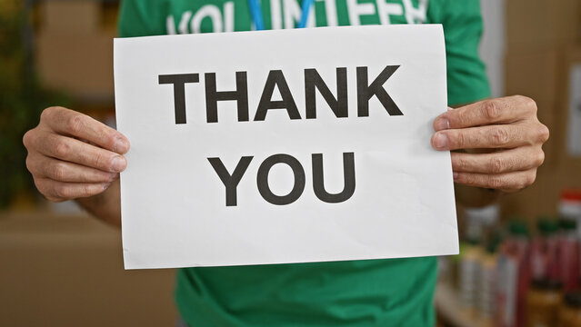 Young hispanic man volunteer holding thank you banner at charity center