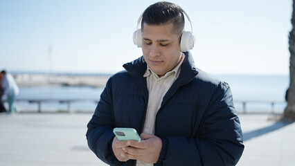 Young hispanic man listening to music at seaside