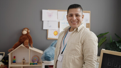 Young hispanic man preschool teacher smiling confident standing at kindergarten