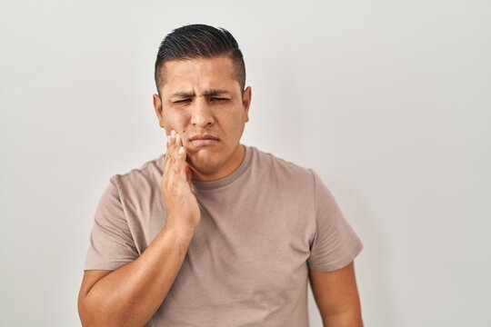 Hispanic young man standing over white background touching mouth with hand with painful expression because of toothache or dental illness on teeth. dentist