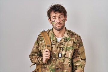 Hispanic young man wearing camouflage army uniform looking sleepy and tired, exhausted for fatigue and hangover, lazy eyes in the morning.