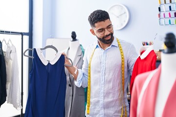 Young arab man tailor smiling confident holding t shirts at tailor shop