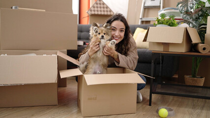 Young hispanic woman with dog sitting on floor playing at new home