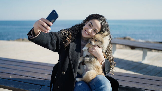 Young hispanic woman with dog smiling confident make selfie by smartphone at seaside - Powered by Adobe