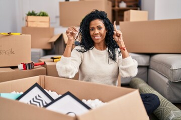 Middle age hispanic woman holding keys of new home smiling with an idea or question pointing finger with happy face, number one