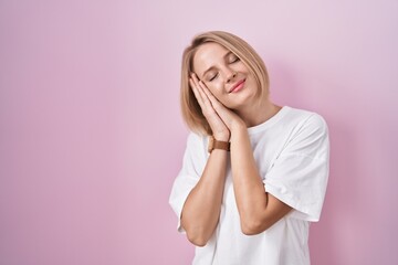 Young caucasian woman standing over pink background sleeping tired dreaming and posing with hands together while smiling with closed eyes.