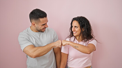 Man and woman couple smiling confident bumping fists over isolated pink background
