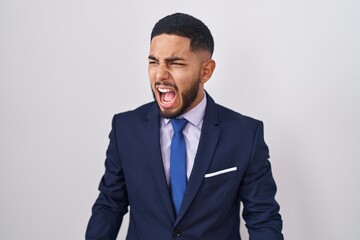 Young hispanic man wearing business suit and tie angry and mad screaming frustrated and furious, shouting with anger. rage and aggressive concept.