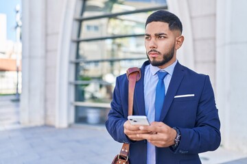 Young latin man business worker using smartphone with serious expression at street