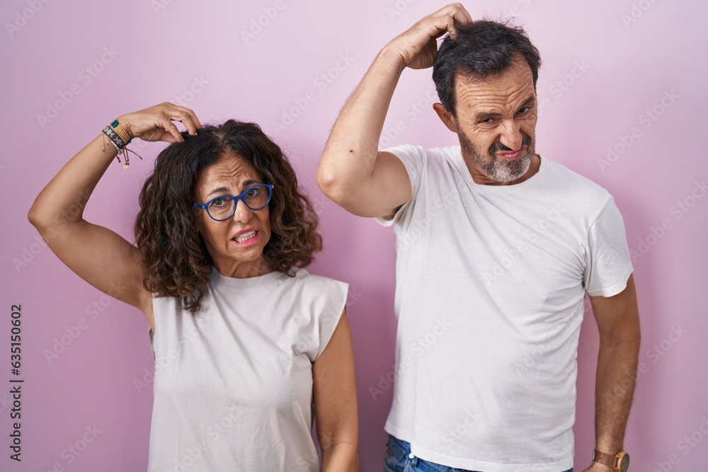 Poster Middle age hispanic couple together over pink background confuse and wondering about question. uncertain with doubt, thinking with hand on head. pensive concept.