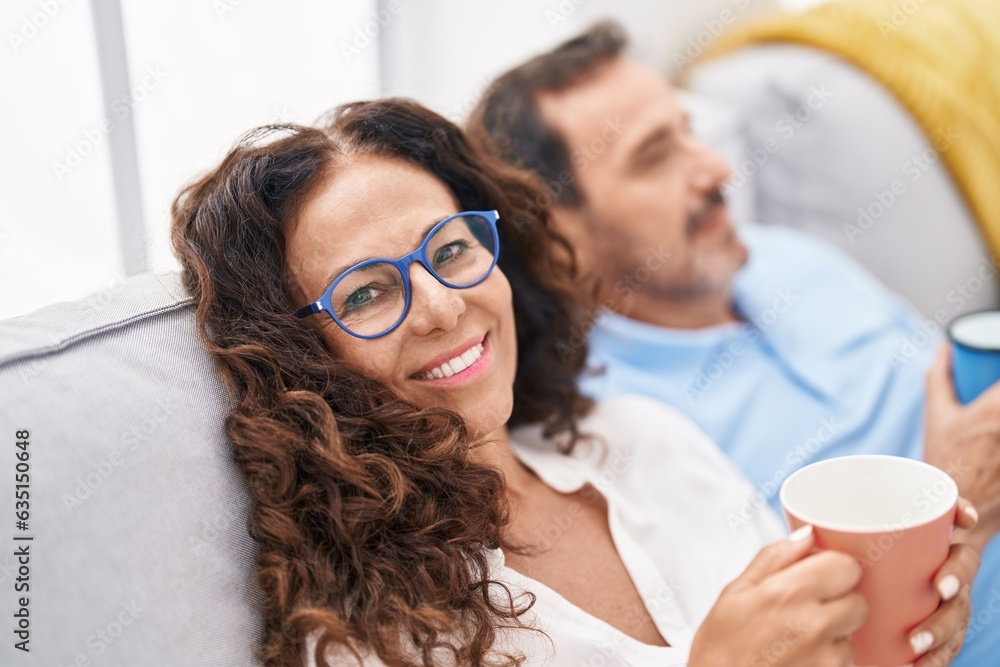 Wall mural Man and woman couple drinking coffee sitting on sofa at home