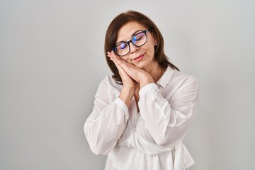 Middle age hispanic woman standing over isolated background sleeping tired dreaming and posing with hands together while smiling with closed eyes.