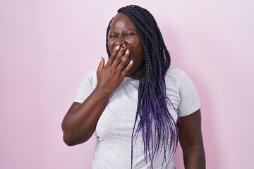 Young african woman standing over pink background bored yawning tired covering mouth with hand....