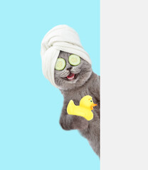 Happy cat with  pieces of cucumber on it eyes  and with towel on it head holds rubber duck behind empty white banner. isolated on blue background