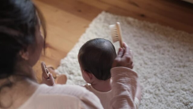 Through the act of grooming her baby, a mother displays the importance of choosing eco-friendly tools, like a wooden comb crafted from eco-friendly materials.
