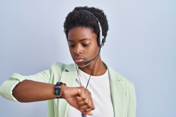 African american woman wearing call center agent headset checking the time on wrist watch, relaxed...