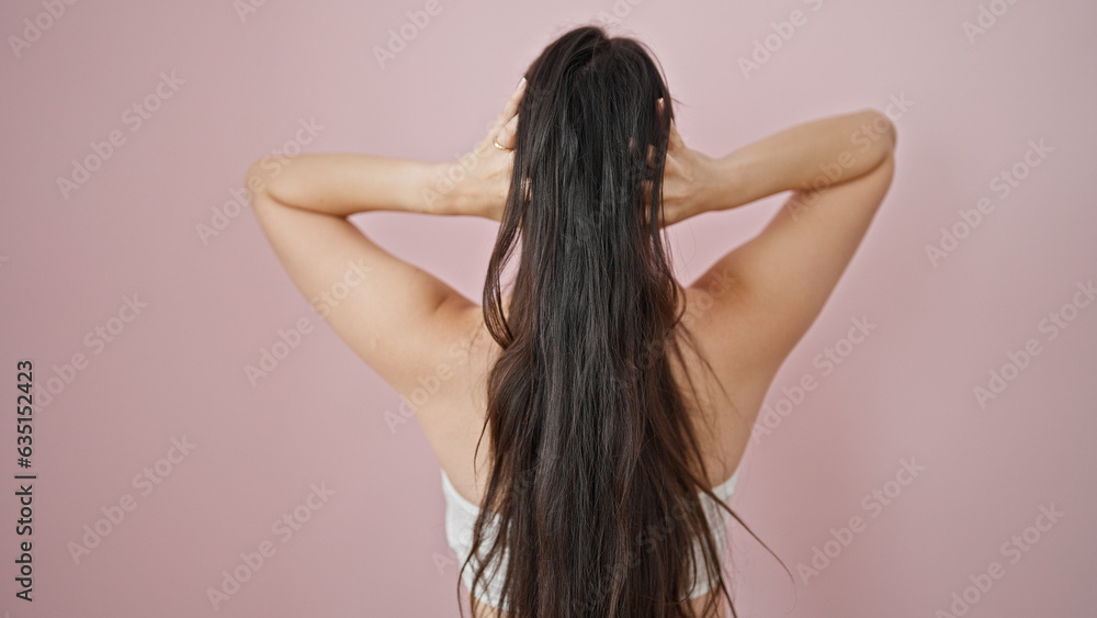 Wall mural Young beautiful hispanic woman touching her hair backwards over isolated pink background