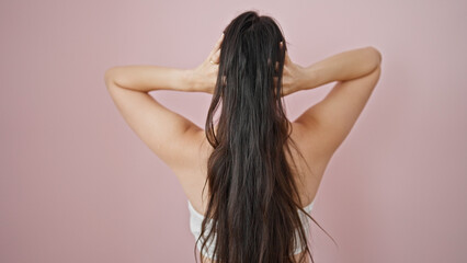 Young beautiful hispanic woman touching her hair backwards over isolated pink background