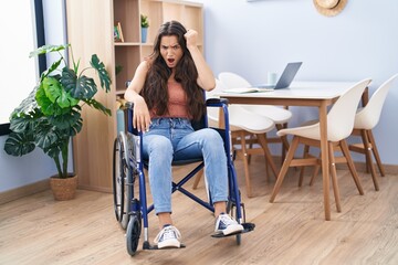 Young teenager girl sitting on wheelchair at the living room annoyed and frustrated shouting with...