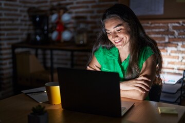 Young teenager girl working at the office at night happy face smiling with crossed arms looking at the camera. positive person.